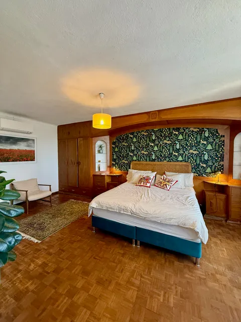 A closer view of the primary bedroom's bed and patterned wallpaper alcove