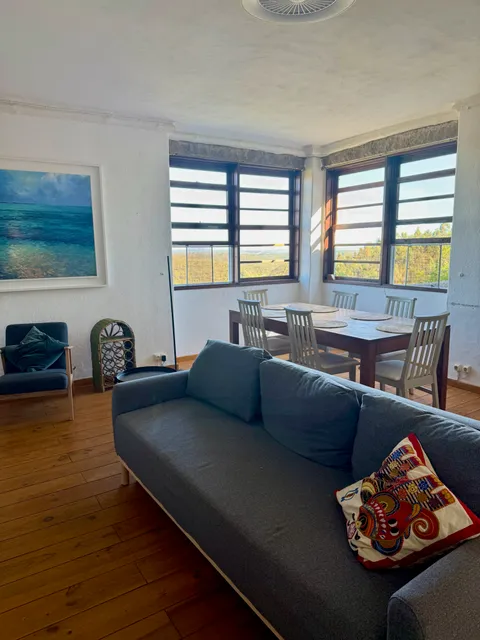 Living and dining area with a sofa, dining table and windows looking over the hills