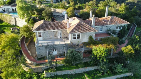 Aerial view of the family home's tiled roofs, courtyards and pool, surrounded by gardens and hills